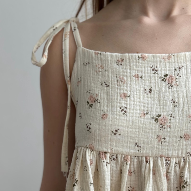 Op de afbeelding: Cr&egrave;mekleurige top met bloemenprint en strikbandjes. De stof heeft een getextureerde, gewatteerde uitstraling en is versierd met kleine roze en bruine bloempatronen. De top heeft een vierkante halslijn en een geplooid, gelaagd ontwerp.