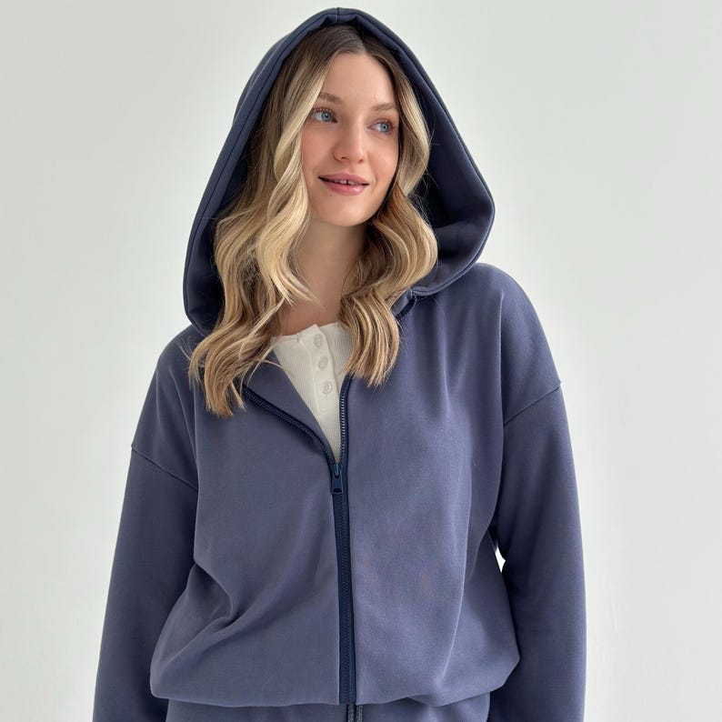 May include: A blue zip-up hoodie with a matching hood and a white shirt underneath. The hoodie has a full-length zipper and is made of a soft material. The model is wearing the hoodie.