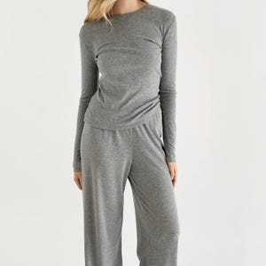Könnte beinhalten: Ein graues Rippstrick-Langarm-Oberteil und eine passende Hose mit weitem Bein. Das Outfit besteht aus einem weichen, bequemen Material. Das Oberteil hat einen Rundhalsausschnitt und die Hose hat eine lockere Passform. Das Outfit eignet sich zum Entspannen oder für Freizeitkleidung.