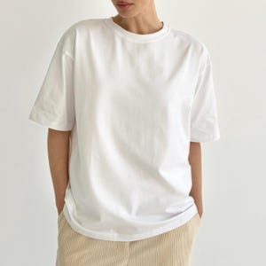 May include: A plain white, short-sleeved t-shirt with a crew neck. The shirt has a relaxed fit and is made of a soft, opaque fabric. The model is wearing the shirt with beige corduroy pants.