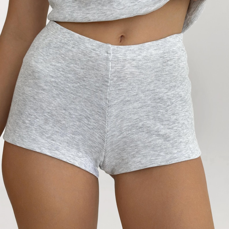 May include: Light gray ribbed knit shorts. The shorts are a basic style with a high waist and a comfortable fit. The fabric has a textured appearance. The shorts are part of a matching set.
