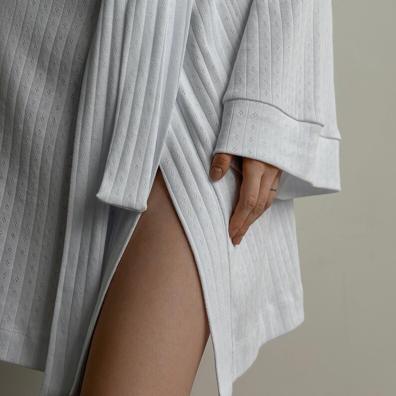 May include: A light blue, long-sleeved robe with a ribbed texture and a high slit. The robe has a relaxed fit with wide sleeves and a subtle pattern of small, evenly spaced perforations. The sleeve cuffs are finished with a contrasting trim.