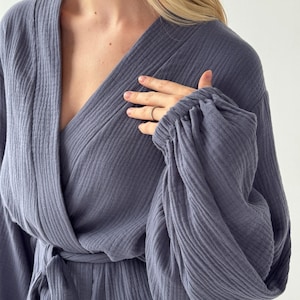 May include: A slate blue robe with a wrap-around design and a tie at the waist. The robe features long sleeves with gathered cuffs. The fabric has a textured, ribbed appearance. The neckline is a deep V-shape.