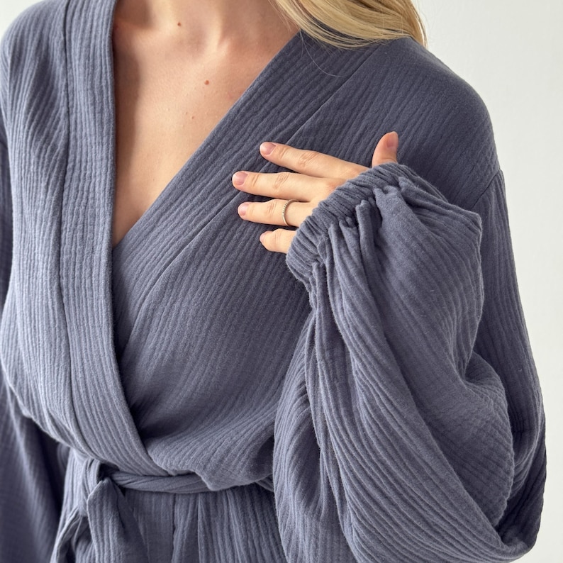 May include: A slate blue robe with a wrap-around design and a tie at the waist. The robe features long sleeves with gathered cuffs. The fabric has a textured, ribbed appearance. The neckline is a deep V-shape.
