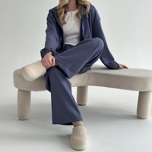 May include: A casual ensemble featuring a blue hooded jacket, matching wide-leg pants, and a white top. The outfit is paired with beige, fuzzy slippers. The clothing set is designed for comfort and relaxation.