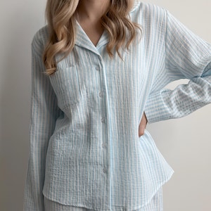Op de afbeelding: Lichtblauw en wit gestreepte pyjama set. Het button-down shirt met lange mouwen heeft een borstzak en een klassieke kraag. De stof lijkt een zacht, getextureerd materiaal te zijn. De pyjama is een comfortabele nachtkleding.