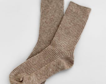 May include: A pair of light brown, ribbed knit socks featuring a vertical texture throughout the leg and foot. The socks have a standard crew length with a reinforced cuff at the top and a defined heel and toe section in a matching tone.