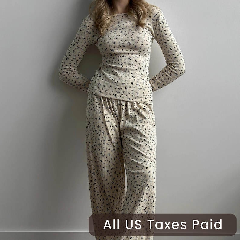 May include: A beige floral-print pajama set. The long-sleeved top and pants feature a delicate pattern of small, dark-colored flowers. The set is made of a soft, comfortable material. The text "ALL US Taxes Paid" is at the bottom of the image.