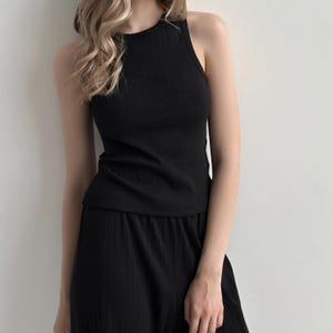 以下が含まれることがあります： 黒のリブ編みタンクトップとマッチするボトムス。ノースリーブのトップスはハイネックです。ボトムスはスカートまたはワイドパンツのようです。この衣装は柔らかく、質感のある生地で作られています。