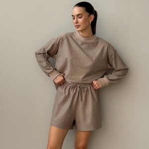 Puede incluir: Conjunto de ropa de estar por casa de dos piezas en color beige neutro. La parte superior de manga larga y los pantalones cortos a juego presentan un sutil estampado de puntos. La parte superior tiene cuello redondo y pu&ntilde;os acanalados, mientras que los pantalones cortos tienen cintura con cord&oacute;n.