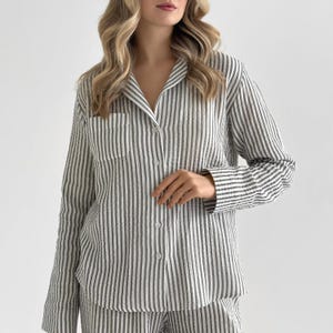 Op de afbeelding: Een tweedelige pyjamaset in een verticaal gestreept patroon van wit en olijfgroen. De button-down shirt met lange mouwen heeft een borstzak en een reverskraag. De stof lijkt een zacht, lichtgewicht materiaal te zijn.