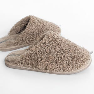 Peut inclure: Deux pantoufles duveteuses de couleur taupe, d'aspect doux et textur&eacute;. Les pantoufles ont un bout arrondi et un profil bas, sugg&eacute;rant un design confortable pour un usage int&eacute;rieur. Le mat&eacute;riau semble &ecirc;tre un tissu doux et moelleux.