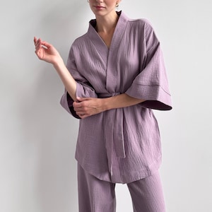 Op de afbeelding: Een mauvekleurige tweedelige loungewear-set bestaande uit een jasje in kimonostijl met wijde driekwartmouwen en een bijpassende ceintuur, gecombineerd met een bijpassende losvallende broek, alles vervaardigd van een textuurrijke mousseline stof.