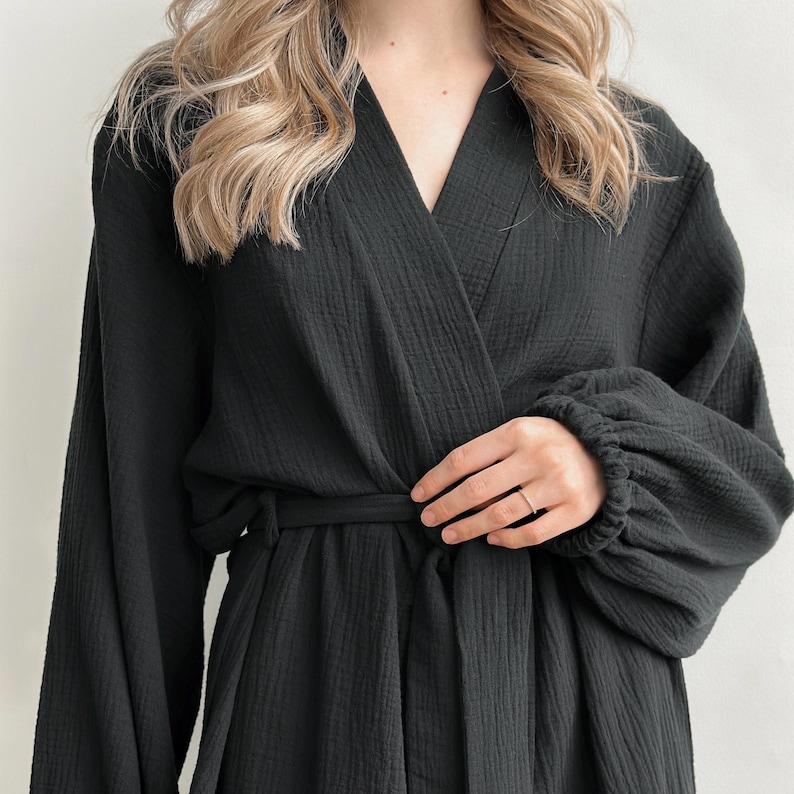 May include: A black robe with long sleeves and a wrap-around design. The robe has a belt at the waist and a V-neckline. The sleeves are gathered at the wrists. The fabric appears to be textured.