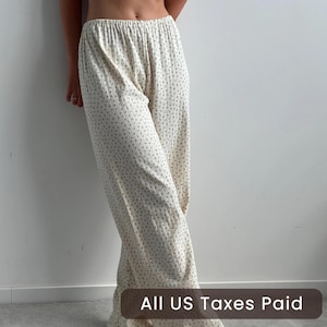 May include: Cream-colored, wide-leg pants with a subtle floral pattern. The pants have a ribbed texture and an elastic waistband. The text "All US Taxes Paid" is visible at the bottom of the image.