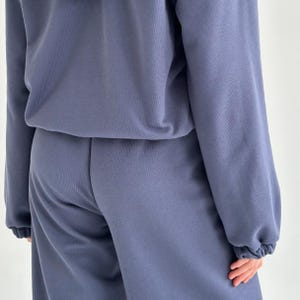 May include: A two-piece matching set in a muted blue color. The top is a long-sleeved sweatshirt with a crew neck. The pants are a relaxed fit with a drawstring waist. The fabric appears to be a soft, comfortable material.