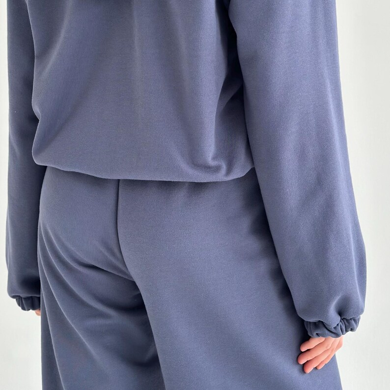 May include: A two-piece matching set in a muted blue color. The top is a long-sleeved sweatshirt with a crew neck. The pants are a relaxed fit with a drawstring waist. The fabric appears to be a soft, comfortable material.