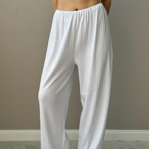 Può includere: Pantaloni da pigiama bianchi a gamba larga con un sottile motivo a pois. I pantaloni hanno una texture a coste e una vita elasticizzata. Il tessuto appare leggero e confortevole, adatto per pigiameria o relax.