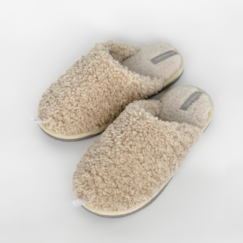 Peut inclure: Une paire de pantoufles beiges et moelleuses avec un ext&eacute;rieur textur&eacute; en forme de sherpa. Les pantoufles ont une semelle gris clair et un int&eacute;rieur doux et rembourr&eacute;. L'&eacute;tiquette &agrave; l'int&eacute;rieur de la pantoufle indique "Twice Home".