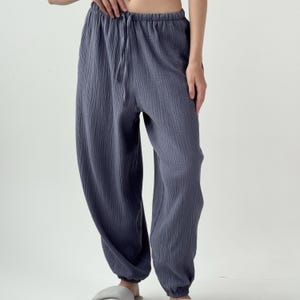 以下が含まれることがあります： 質感のあるシワ加工が施されたダークスレートブルーのパンツ。ゆったりとしたシルエットのこのパンツは、同色のドローストリング付きの伸縮性ウエストバンドと、足首にギャザーを寄せた伸縮性のある裾が特徴です。