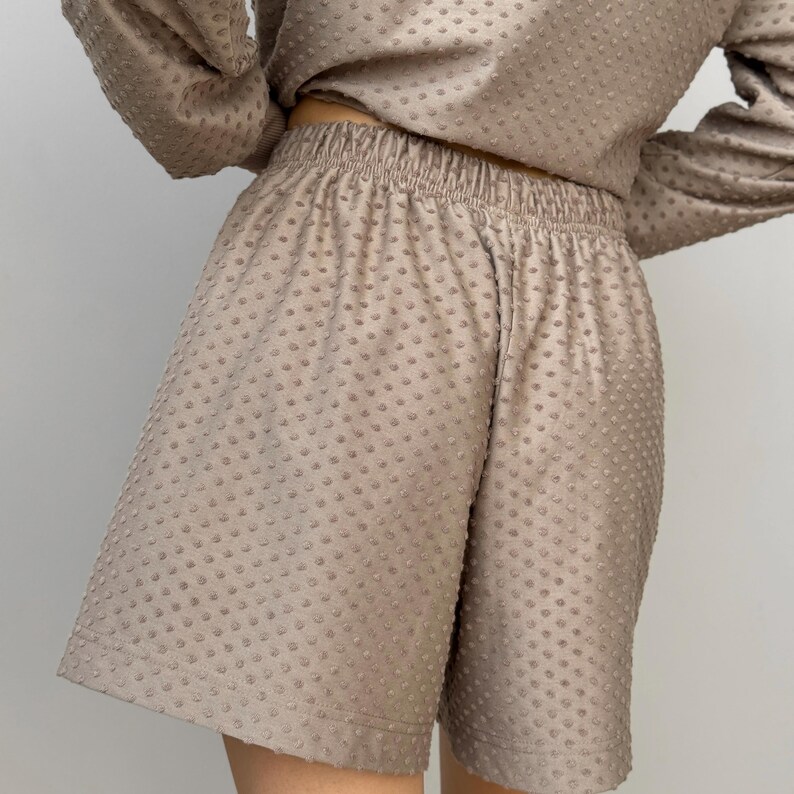 Puede incluir: Un conjunto beige de dos piezas con shorts y una parte superior de manga larga. Los shorts tienen una cintura el&aacute;stica y un ajuste relajado. La tela tiene un patr&oacute;n texturizado y punteado. La parte superior es corta y las mangas son largas.