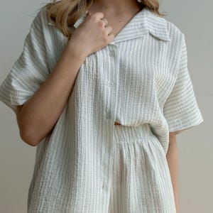 May include: A light green and white striped pajama set. The set includes a short-sleeved button-down shirt and matching shorts. The fabric has a textured, crinkled appearance.