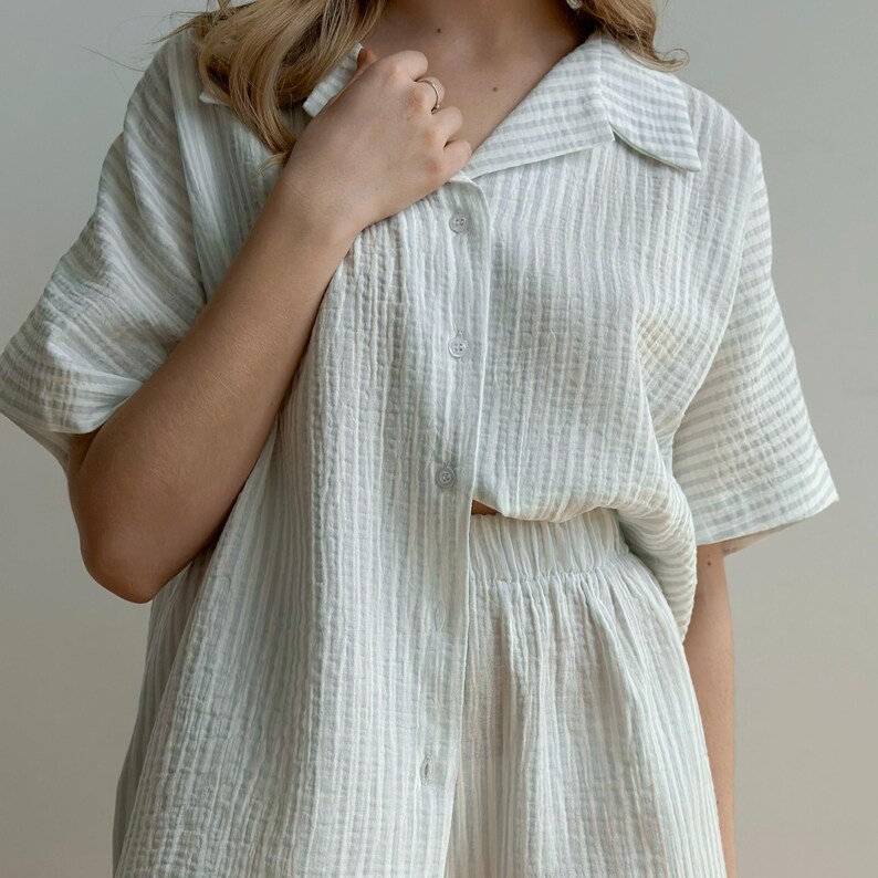 May include: A light green and white striped pajama set. The set includes a short-sleeved button-down shirt and matching shorts. The fabric has a textured, crinkled appearance.
