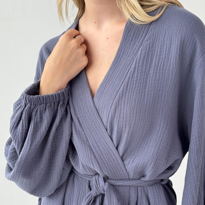 May include: A periwinkle blue robe with a wrap-around design and a tie closure at the waist. The robe features long sleeves with elastic cuffs and a textured fabric. The neckline is a deep V-shape.