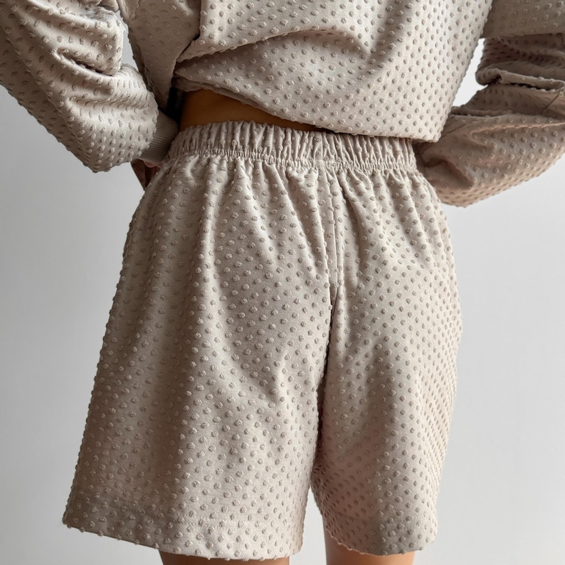 Puede incluir: Conjunto de dos piezas beige con una parte superior de manga larga y pantalones cortos a juego. La tela tiene un patr&oacute;n texturizado con puntos. Los pantalones cortos tienen cintura el&aacute;stica. El conjunto es de color neutro.