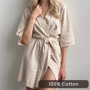 May include: A beige floral print wrap dress with a tie waist. The dress has short sleeves and a V-neckline. The text "100% Cotton" is displayed at the bottom of the image.