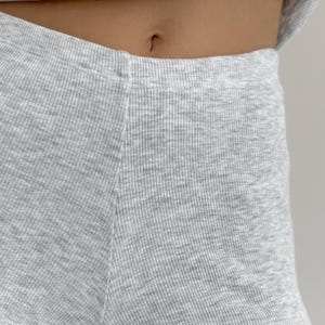 May include: Close-up of light gray ribbed knit shorts. The fabric has a textured appearance with vertical ribbing. The shorts are high-waisted and appear to be part of a matching set. The image is well-lit, highlighting the fabric's details.