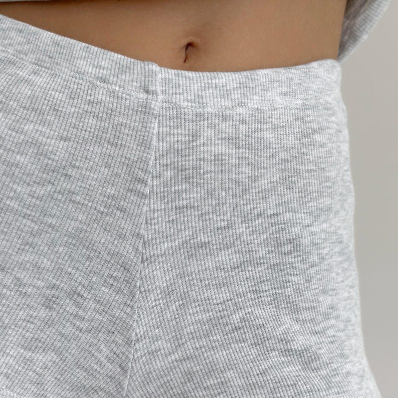 May include: Close-up of light gray ribbed knit shorts. The fabric has a textured appearance with vertical ribbing. The shorts are high-waisted and appear to be part of a matching set. The image is well-lit, highlighting the fabric's details.