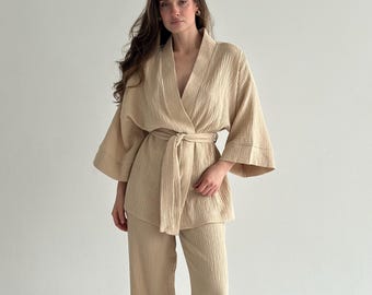 May include: A beige two-piece set consisting of a long-sleeved kimono-style jacket with a tie-waist belt and matching wide-leg trousers. The garment is crafted from a textured, crinkled fabric with a V-neckline and loose, flowing sleeves.