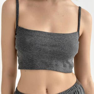 May include: A dark gray, ribbed-knit crop top with thin shoulder straps. The top has a square neckline and appears to be part of a matching set. The fabric has a vertical ribbed texture.