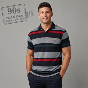 May include: A short-sleeved polo shirt featuring horizontal stripes in navy blue, grey, red, and dark green. The shirt has a collar with a button placket and a small embroidered logo on the left chest. Text in the corner reads 90s Paul & Shark Yachting Polo Shirt.