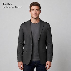 May include: A dark charcoal gray blazer with a notched lapel, two front buttons, and two flap pockets. The text Ted Baker Endurance Blazer is visible in the upper left corner. The garment is worn over a plain dark gray t-shirt and dark blue jeans.
