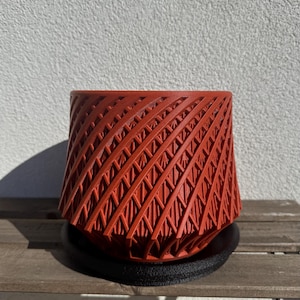 May include: A red, geometrically patterned planter with a black base. The planter has a unique, swirling design.