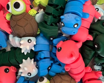 May include: A collection of colorful, segmented, articulated animal toys. The toys are made of plastic and feature a variety of animals, including a turtle, a hippopotamus, a chameleon, and a dinosaur. The toys are all brightly colored and have large, expressive eyes.