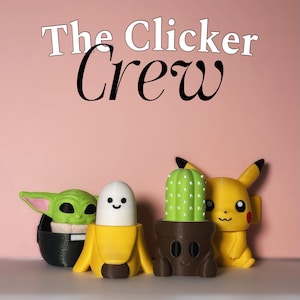 Pode incluir: Uma coleção de figuras coloridas impressas em 3D, incluindo um Baby Yoda verde, uma banana com um rosto sorridente, um cacto em vaso e um Pikachu amarelo. O texto "The Clicker Crew" é exibido acima das figuras contra um fundo rosa.