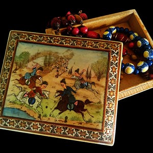 May include: An open wooden box with a hand-painted lid depicting a polo match scene. The box is decorated with an ornate border. Inside the box are several beaded necklaces in red, blue, and yellow. The background is black.