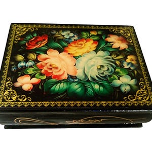 Pode incluir: Uma caixa lacada preta com um design floral. A tampa é adornada com um arranjo vibrante de rosas e outras flores em tons de vermelho, amarelo e branco, sobre um fundo escuro. As bordas são aparadas com filigrana dourada.
