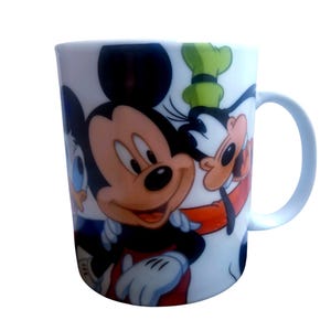 Può includere: Tazza in ceramica bianca con Topolino, Paperino e Pippo. La tazza ha un manico azzurro chiaro ed è decorata con personaggi dei cartoni animati colorati. Una classica tazza da caffè a tema Disney.