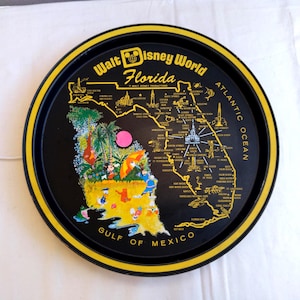 May include: A circular black tray with a yellow rim, displaying a map of Florida and the words "Walt Disney World Florida". The map is decorated with Disney characters and landmarks. A vintage souvenir item.