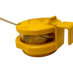 Puede incluir: Un tarro de especias de plástico amarillo con un recipiente de vidrio transparente en el interior. El tarro tiene una tapa con un asa pequeña y una cuchara incorporada. El tarro tiene un asa en el lateral.