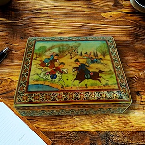 May include: A rectangular wooden box with a detailed painting on the lid depicting a polo match with riders on horseback. The box has a decorative border with intricate patterns and is set on a wooden surface.
