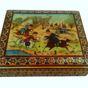 May include: A rectangular, decorative box with a hand-painted scene of horse riders playing polo. The box features a detailed border with floral and geometric patterns. The artwork depicts figures in colorful attire on horseback, set against a landscape.