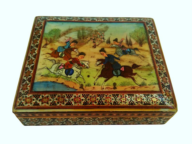 May include: A rectangular, decorative box with a hand-painted scene of horse riders playing polo. The box features a detailed border with floral and geometric patterns. The artwork depicts figures in colorful attire on horseback, set against a landscape.