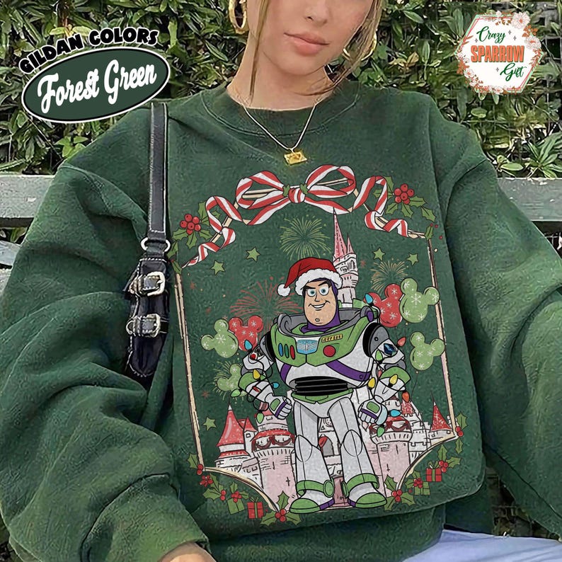 May include: Forest green sweatshirt featuring a festive design with Buzz Lightyear in a Santa hat, surrounded by Christmas decorations and a castle. The sweatshirt has the text "Gildan Colors Forest Green" on the upper left.