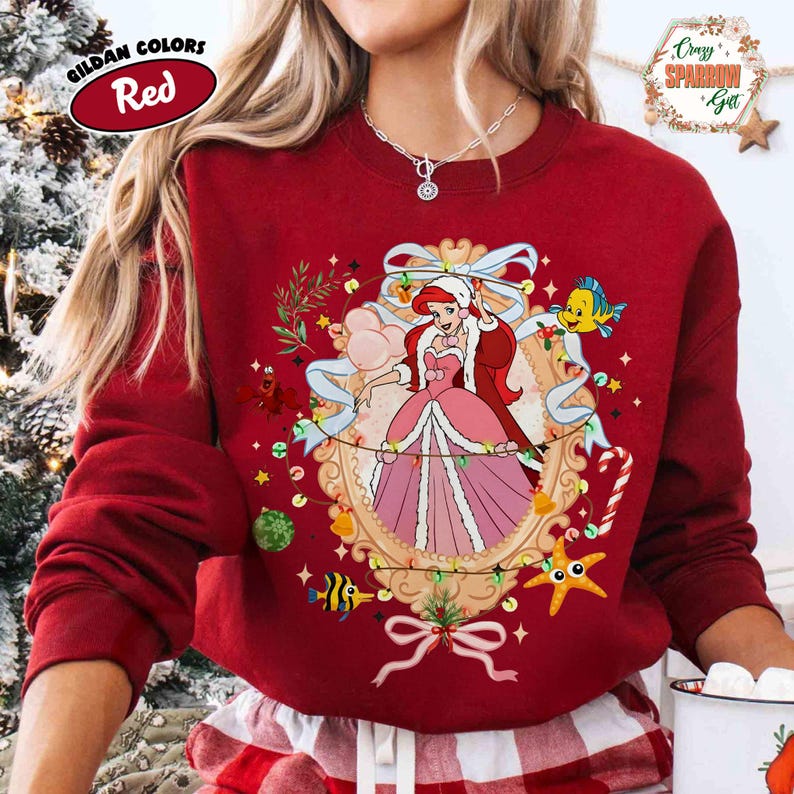 May include: Red sweatshirt featuring a framed illustration of a princess in a pink dress, surrounded by festive decorations. The sweatshirt has the text "Gildan Colors Red" on the upper left and "Crazy Sparrow Gift" on the upper right.