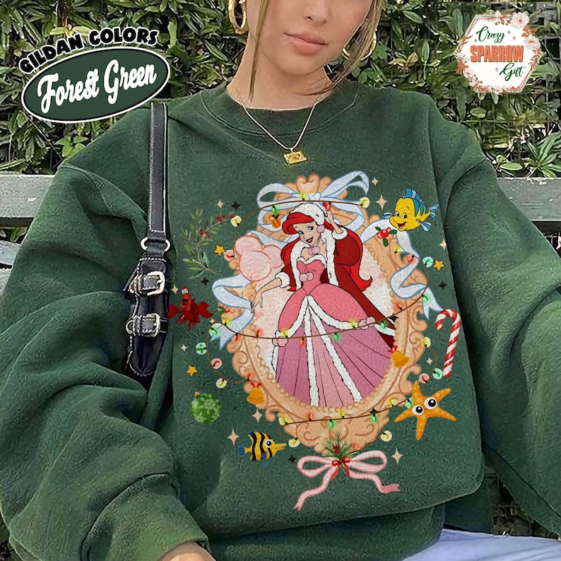 May include: Forest green sweatshirt featuring a framed illustration of a princess in a pink dress, with a red cape and a white hat. The illustration includes a yellow fish, a starfish, and candy canes. The sweatshirt has the text "GILDAN COLORS Forest Green".